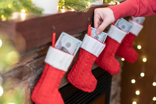 Woman putting american dollars in сhristmas red socks for gifts on the fireplace in bokeh lights.