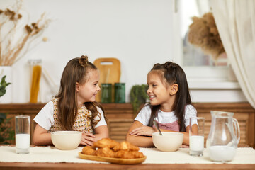 Obraz na płótnie Canvas Cute healthy little children girls having breakfast - fresh delicious croissants and milk in the kitchen.