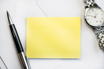 a yellow note sheet is placed on a light background near the wristwatch and pen. Business and...