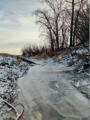 frozen river with snow covered banks and trees with fallen leaves