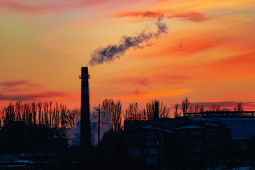 Fototapeta premium High and wide chimney, a pipe with a large amount of smoke and substances released into the atmosphere. Part of a factory or enterprise that pollutes the environment in a snowy and frosty winter near 