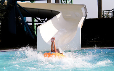 Young woman on rubber ring going down slide in aqua park