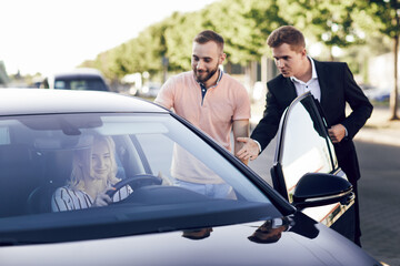 The seller shows buyers a new car. Young man and woman choose a car outdoors. Test drive a new car