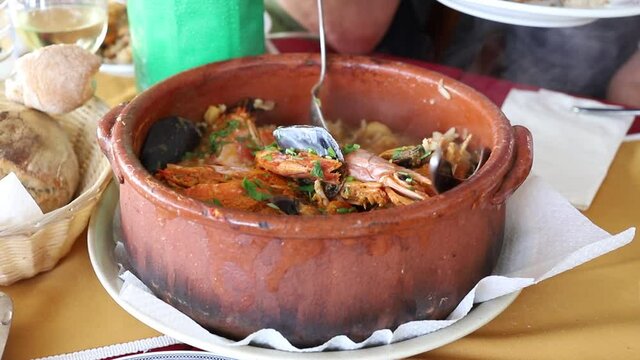 people eating typical portuguese dish rice with seafood in red ceramic pot in restaurant