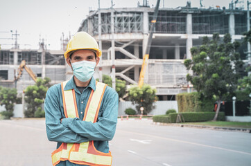 Male construction engineer with arms folded in front of a building at a construction site