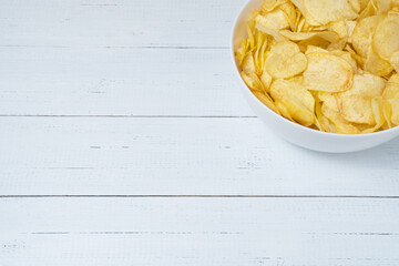 Bowl of natural potato chips on white wooden table with copy space.