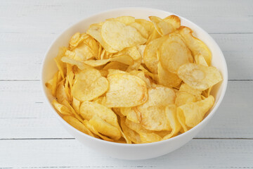 Bowl of natural potato chips on white wooden table.