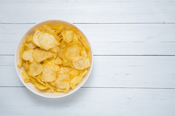Bowl of tasty and crispy potato chips on white wooden table with copy space, top view.