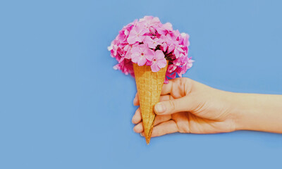 Colorful image of hand with cone and pink flowers as ice cream over a blue background