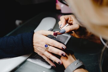 Close up with unrecognizable hands of manicurist applying red gel polish on client's nails. professional, beauty concept.