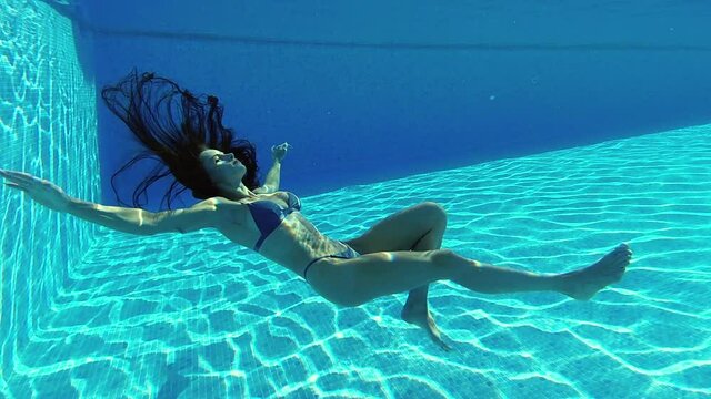 Relaxed serene young woman dives falling into swimming pool depth