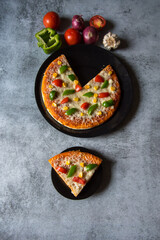 Top view of a slice of pizza served from a whole pizza on a plate along with ingredients.