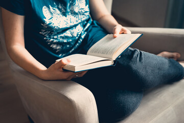 A young pretty woman sits on an armchair and reads a book.Close-up of female hands holding an open book. Cozy home