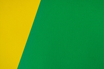 Beautiful background of two unequal parts of colored paper yellow and green. Sheets of blank yellow and green paper with fine texture separated by a sloping border.
