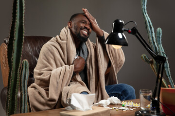 Terrible headache. African-american man wrapped in a plaid looks sick, ill sitting on armchair at home indoors. Healthcare and medicine, ill prevention, seasonal illness symptoms and self-protection.