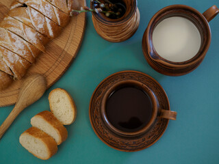 Flat lay of beautifully served breakfast in handmade earthenware against a green background. Fresh delicious pastries with bird cherry filling, a cup of hot aromatic tea, a crispy French baguette