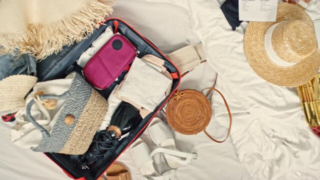 Top view flat lay of hat, sunglasses, swimsuit and half-packed suitcase lying on bed
