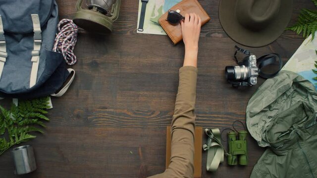 Time-lapse top view of unrecognizable woman arranging travel gear and accessories on wooden table, then putting photos from recent trips in center