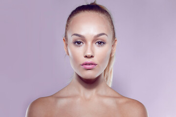 Front closeup portrait of a blonde beautiful girl with ponytail hairstyle and bare shoulders, on purple background.