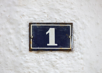 Street number one. House address metal sign on whitewashed wall.