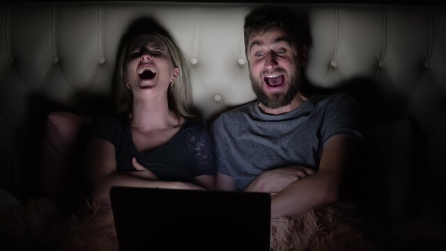 Man and woman, young couple watching funny movie on laptop in bed before going to bed