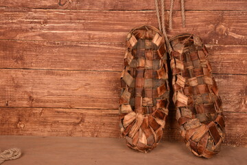 Birchen woven bast shoes hang on a log wall.