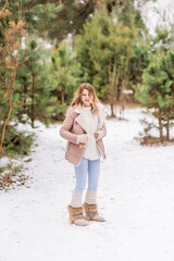 Beautiful young woman in jeans and pink jacket laughing in the winter forest