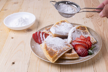Closeup of sliced waffles with fresh strawberries and sprinkled with powdered sugar