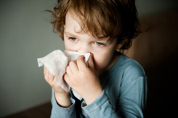 Cute boy blowing nose into a handkerchief.