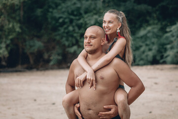 Fototapeta premium A bald guy carrying a girl on his back, at the beach, outdoors. Phuket. Thailand.