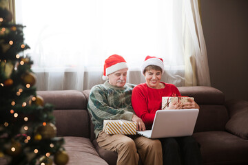 Elderly couple in a Santa's hat    with a Christmas gift using laptop and having video call with friends or relatives at home. Christmas at home