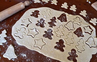Christmas cookie dough stretched and cut with molds in the shape of a gingerbread man, stars, trees and bells with several cutters and a rolling pin next to it