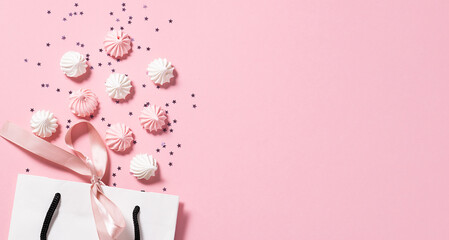 Creative composition with white paper bag with a bow, colorful sweet meringue cookies and shining stars on pink pastel background. Festive shopping and sale concept, copy space for your text.