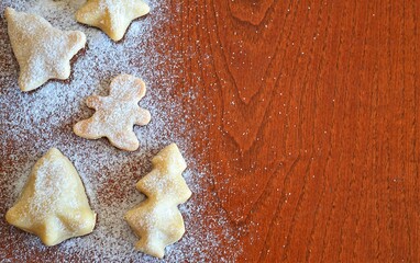 Line of christmas cookies shaped like a gingerbread man, bells, christmas trees and stars on a wooden background with powdered sugar sprinkled