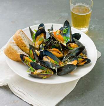 A pint of muscles in their shells, in a white bowl with crusty French bread and a glss of beer