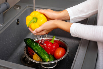 Woman's hand washes vegetables Cooking fresh salad. Fresh vegetables lie in a sink in a modern...