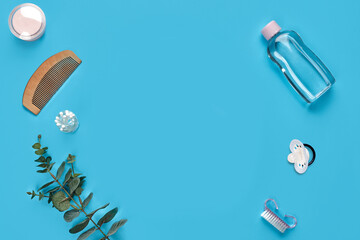 Wooden hair comb, cotton pads, pacifier, bottle with transparent liquid, cotton swabs, brush and green twig on blue background. Close up, copy space