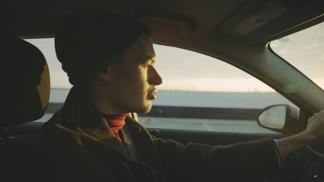 Handsome Guy Driving Car On The Road By The Sea In Golden Hour Sunset - side view, slow motion