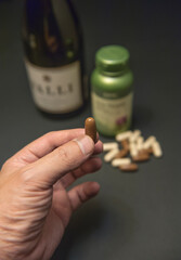 Asian man holding a brown pill on hand with a bottle of liquor and vitamin on black background.