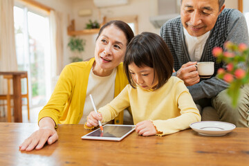 Obraz premium タブレット学習をする孫を見守る祖父母