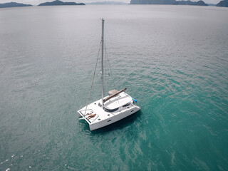 Naklejka premium Young couple relaxing on board of the sail boat anchored in shallow tropical bay. Aerial photo