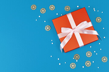 Christmas gift box with ribbon surrounded by seasonal wooden snowflake ornaments and white...