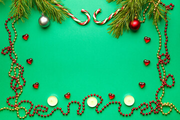 Christmas frame with candles, decorative beads and sprigs of pine with decorations on a green background. Place for an inscription.