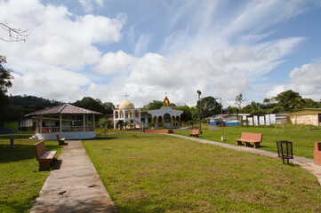 Fototapeta na wymiar village park with green areas, kiosk and church on a sunny day