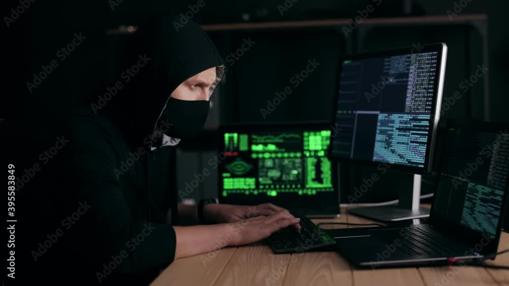 Poster man in mask and hood looking at monitors and waiting for result, hacker breaking system