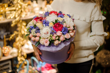 flower arrangement of different flowers in large lilac round box in woman's hand