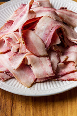 A pile of fresh sliced smoked bacon on a white decorative plate.