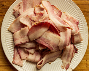 A pile of fresh sliced smoked bacon on a white decorative plate.