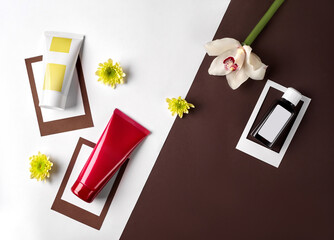 Two cosmetic tubes and plastic bottle with branding area, orchid and chrysanthemum buds against colorful studio background. Close up, copy space