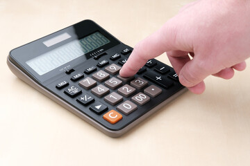 The calculator is on the table and the finger presses the key